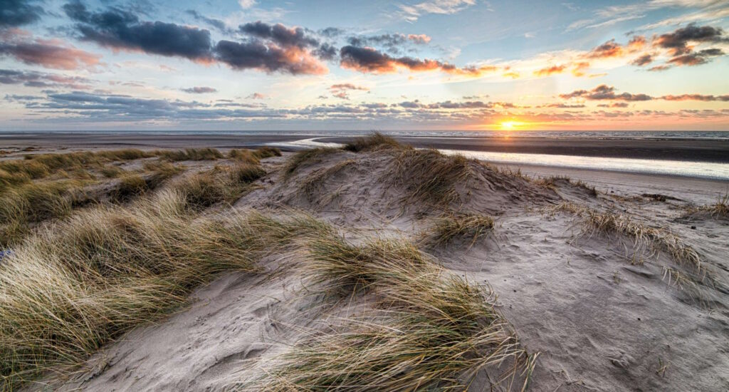 Dünen und Strand, im Hintergrund ist ein Sonnenuntergang zu sehen.