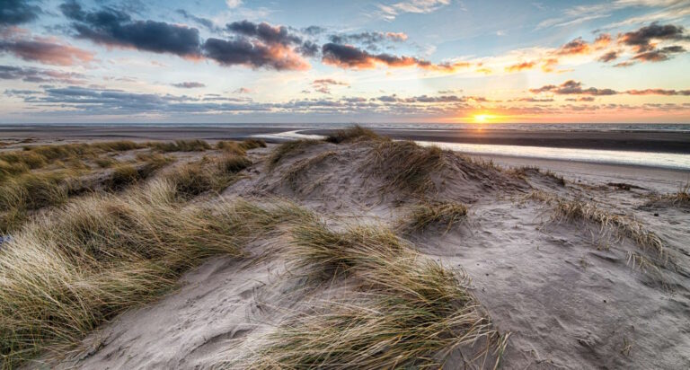 Dünen und Strand, im Hintergrund ist ein Sonnenuntergang zu sehen.