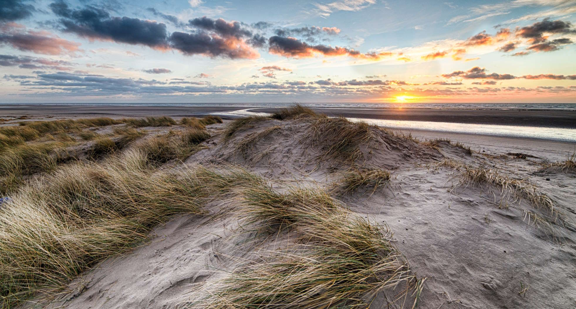 Dünen und Strand, im Hintergrund ist ein Sonnenuntergang zu sehen.